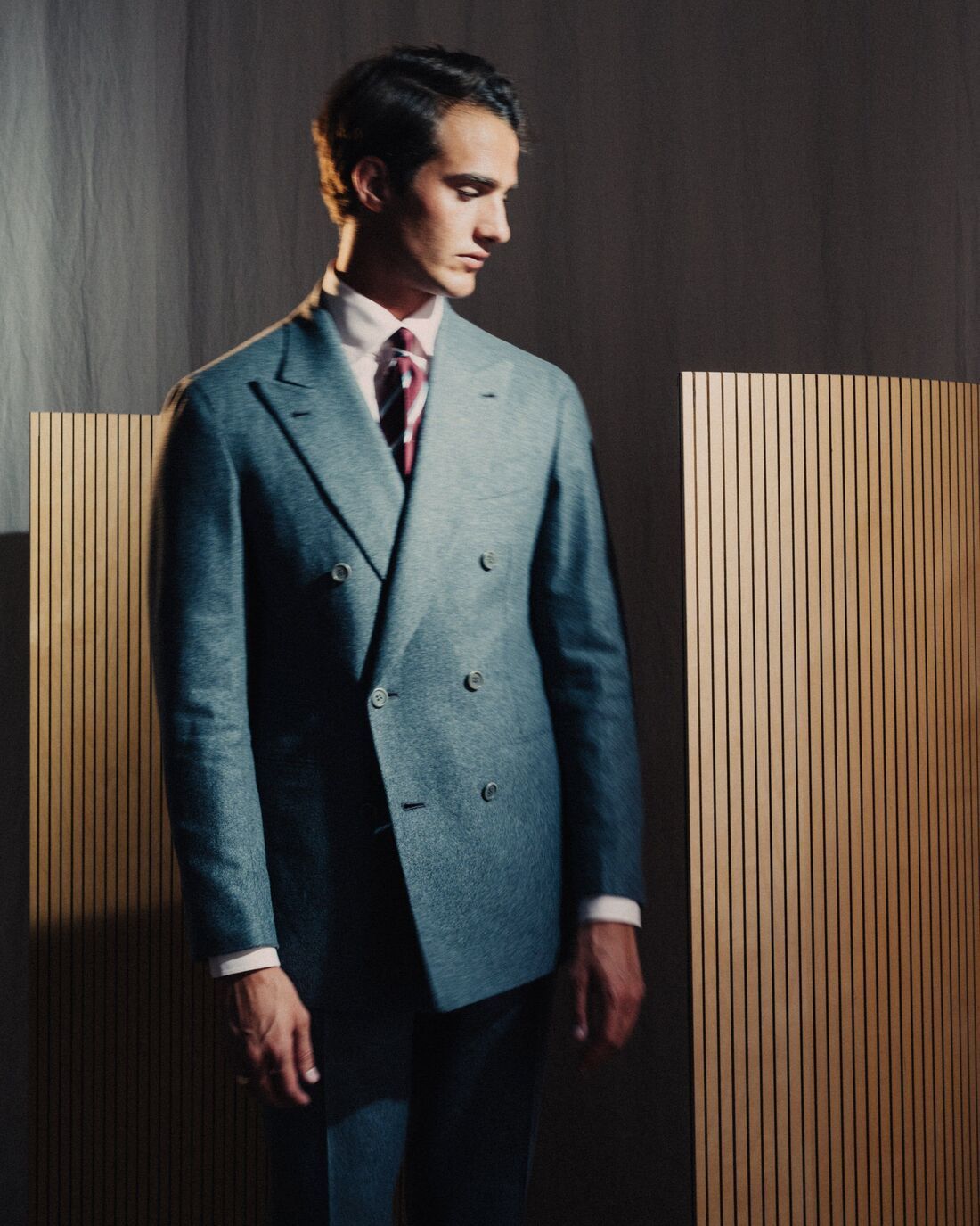 A man dressed in a classic italian double-breasted suit looking away from the camera, with soft glowing light on his face