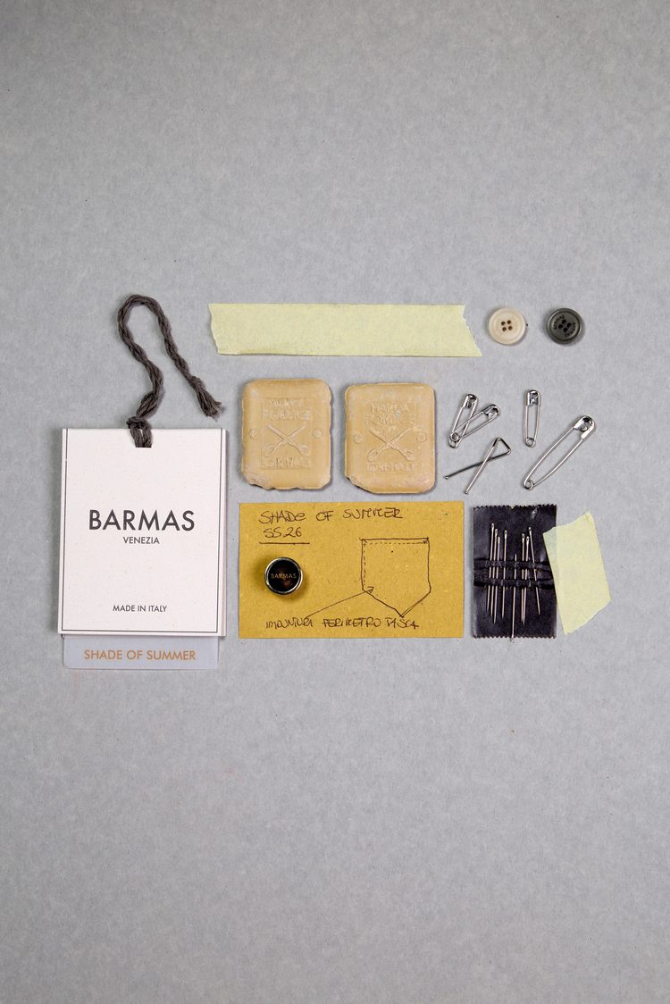 A flat-lay of Barmas Venezia trims on grey card — a hang tag, buttons, pumice stones, safety pins, needles and a hand-sketched pocket design
