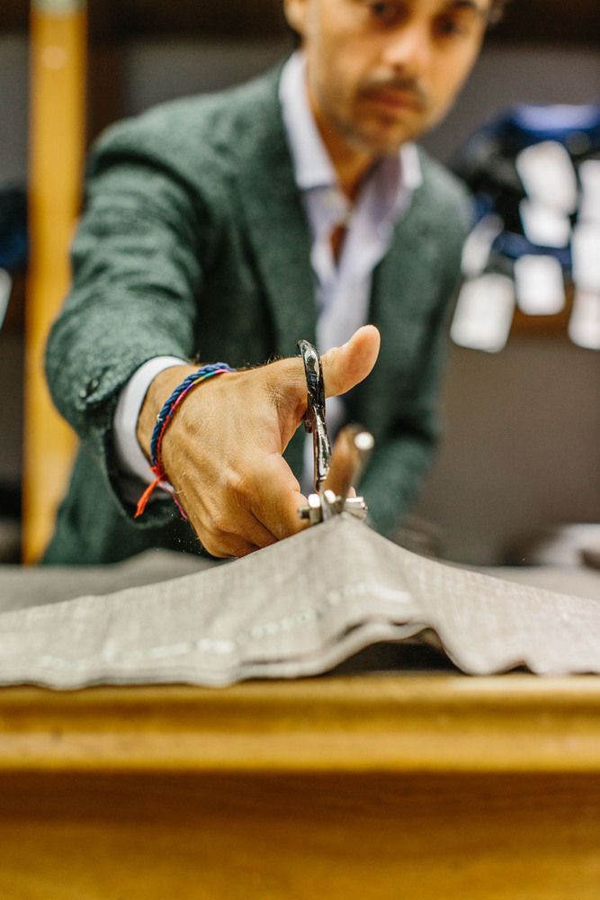 Close-up of a suited man's hand cutting a fabric, his face is visible in the background but out-of-focus