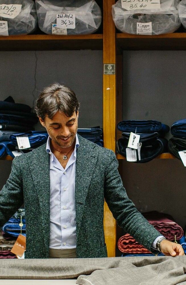 A suited man smiling, lays down a fabric with marked items behind him