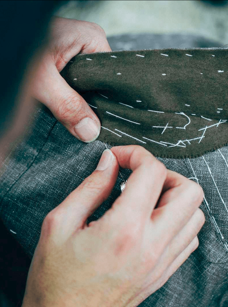 Close-up of hands working away at sewing the inside of a suit
