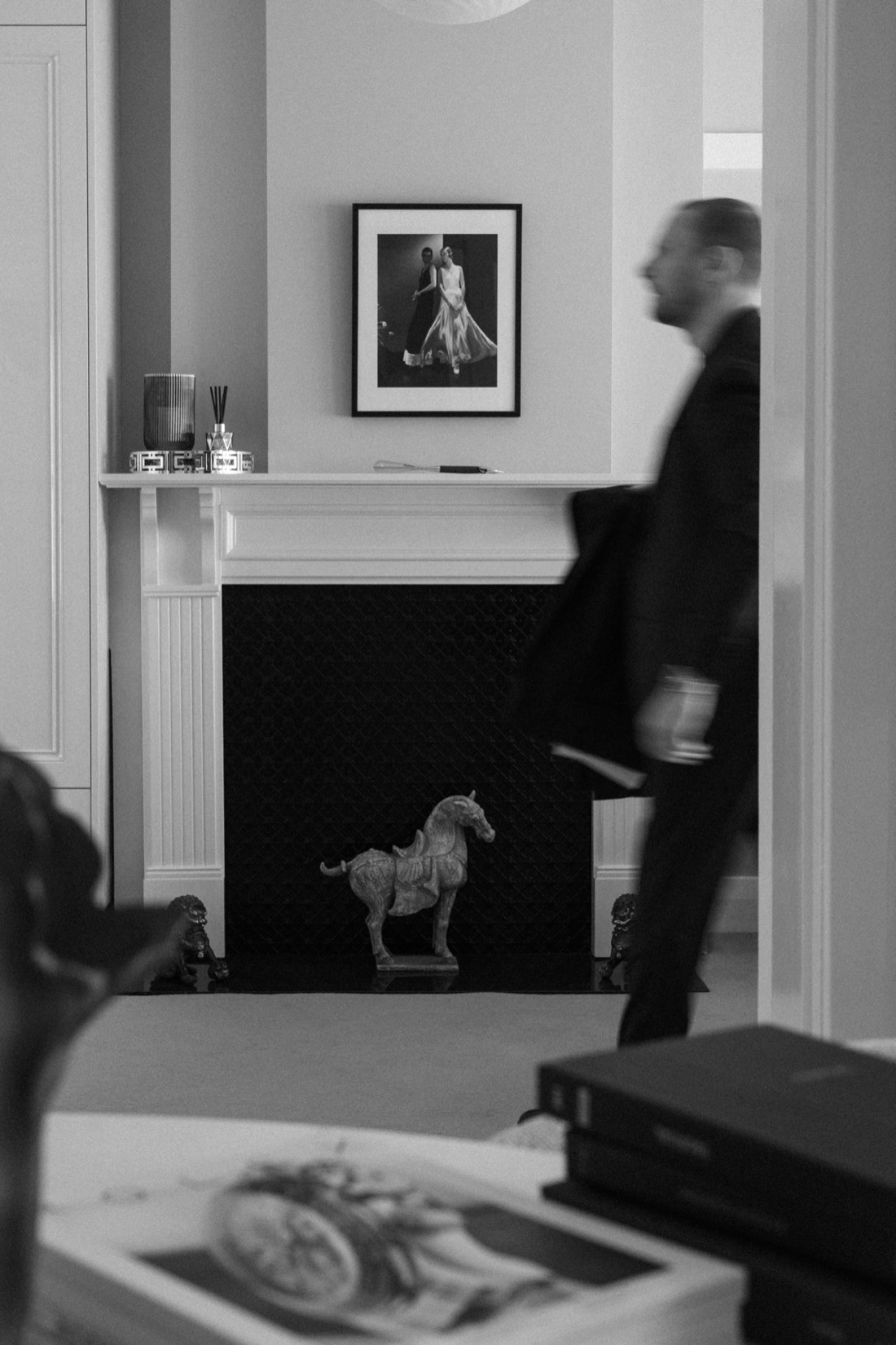 A guest moving through the private Toorak showroom in black and white, past the mantel and a horse sculpture