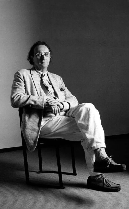 a black & white full portrait of a suited gentleman wearing glasses sitting relaxed on a chair with crossed legs