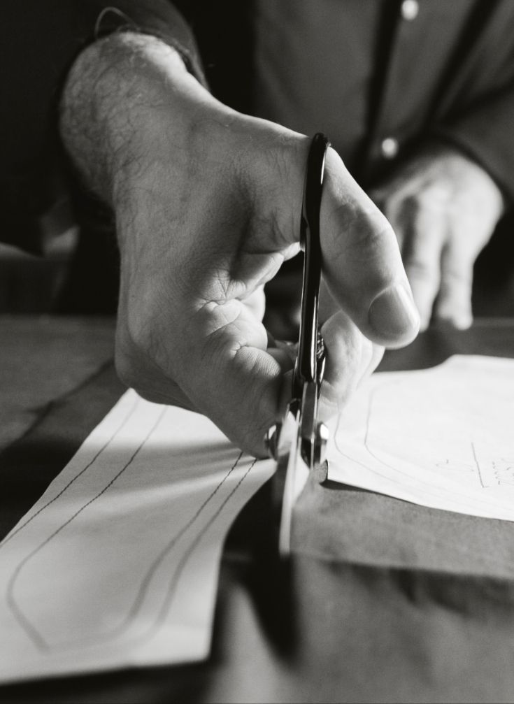 A black & white close-up of a man's hand cutting fabric