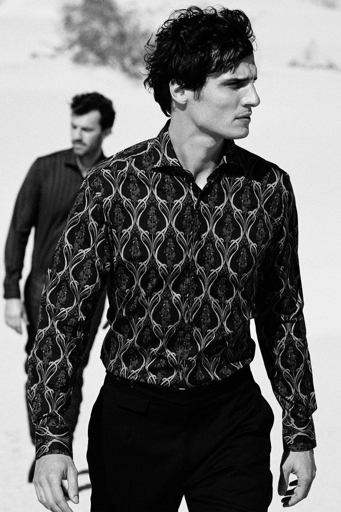 A black & white portrait of a man wearing a patterned shirt staring into the distance